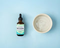 Bee Clear dental hygiene water additive beside a ceramic bowl of water on a pale blue background