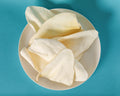 Premium cow ears on a white plate, shot overhead on a teal seamless background