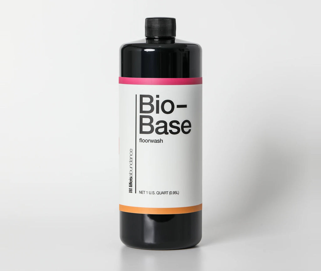 Bio-Base floorwash concentrate, black one-quart bottle with the pink and orange banded label, straight on against a pale studio seamless