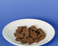 Lamb & Venison Recipe jerky treats on a white plate against a blue background