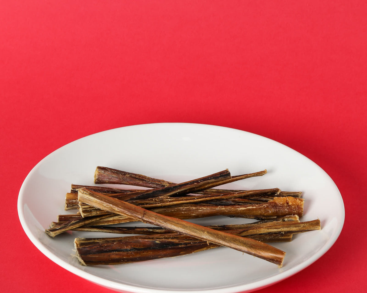 Pork bully sticks piled on a white plate on a red background